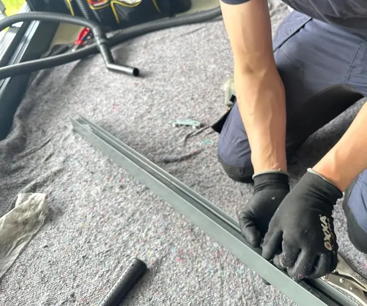 Monteur knielt op een stucloper naast het losgenomen railprofiel van een schuifpui, met tang en stofzuigerslang binnen handbereik